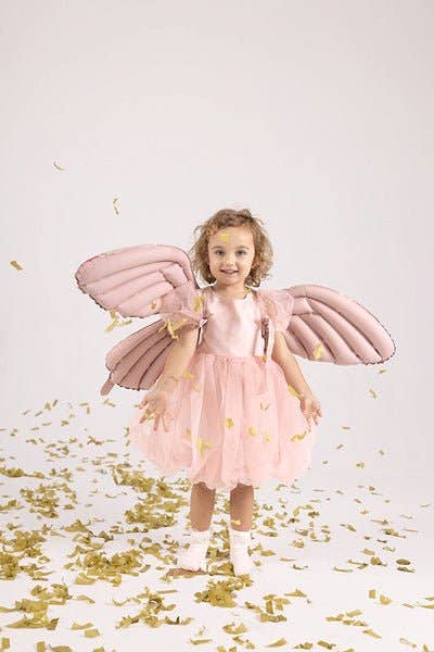 Child in a pink fairy costume with wings standing on a white background with gold confetti.