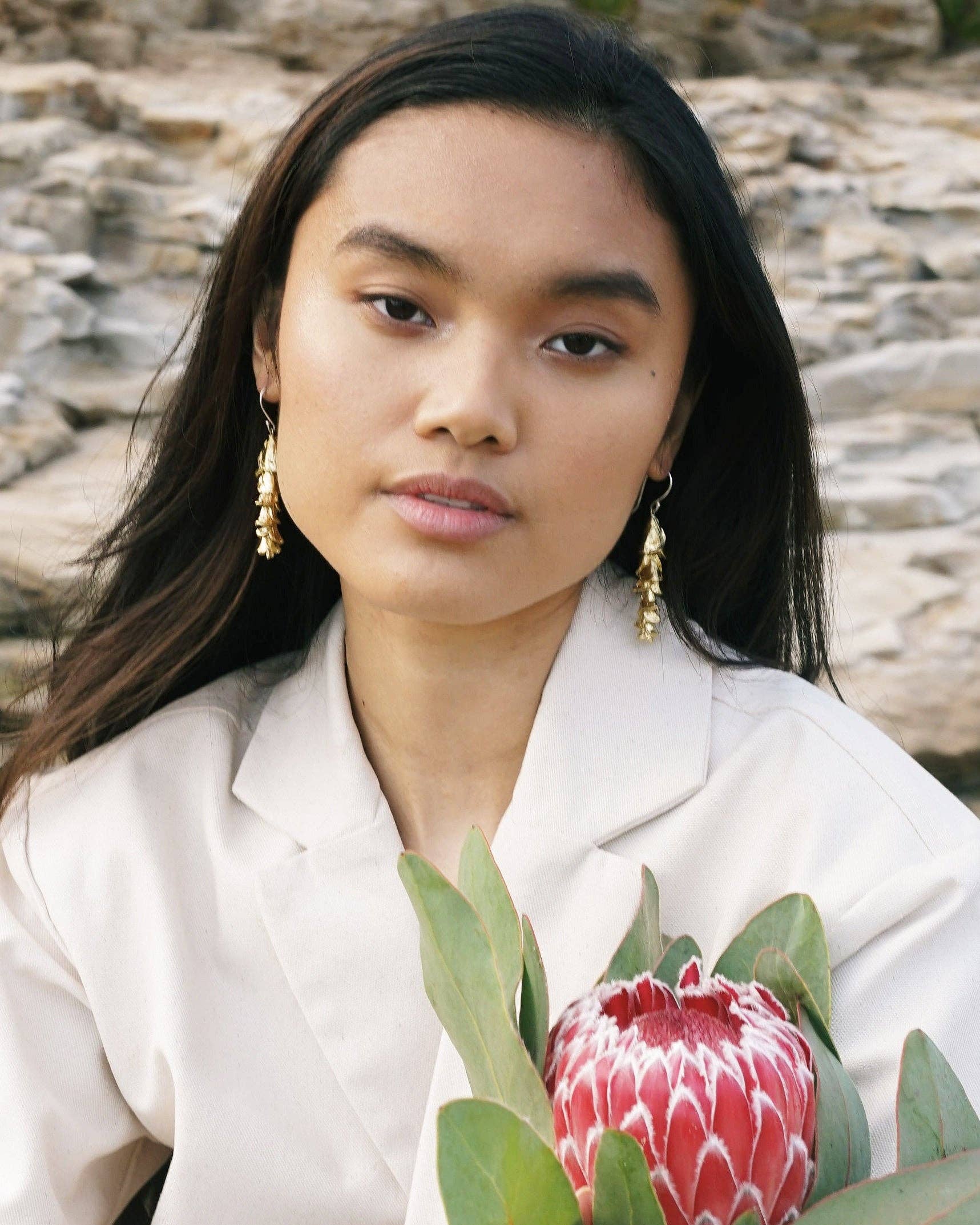 Woman holding a red flower with green leaves against a natural stone background