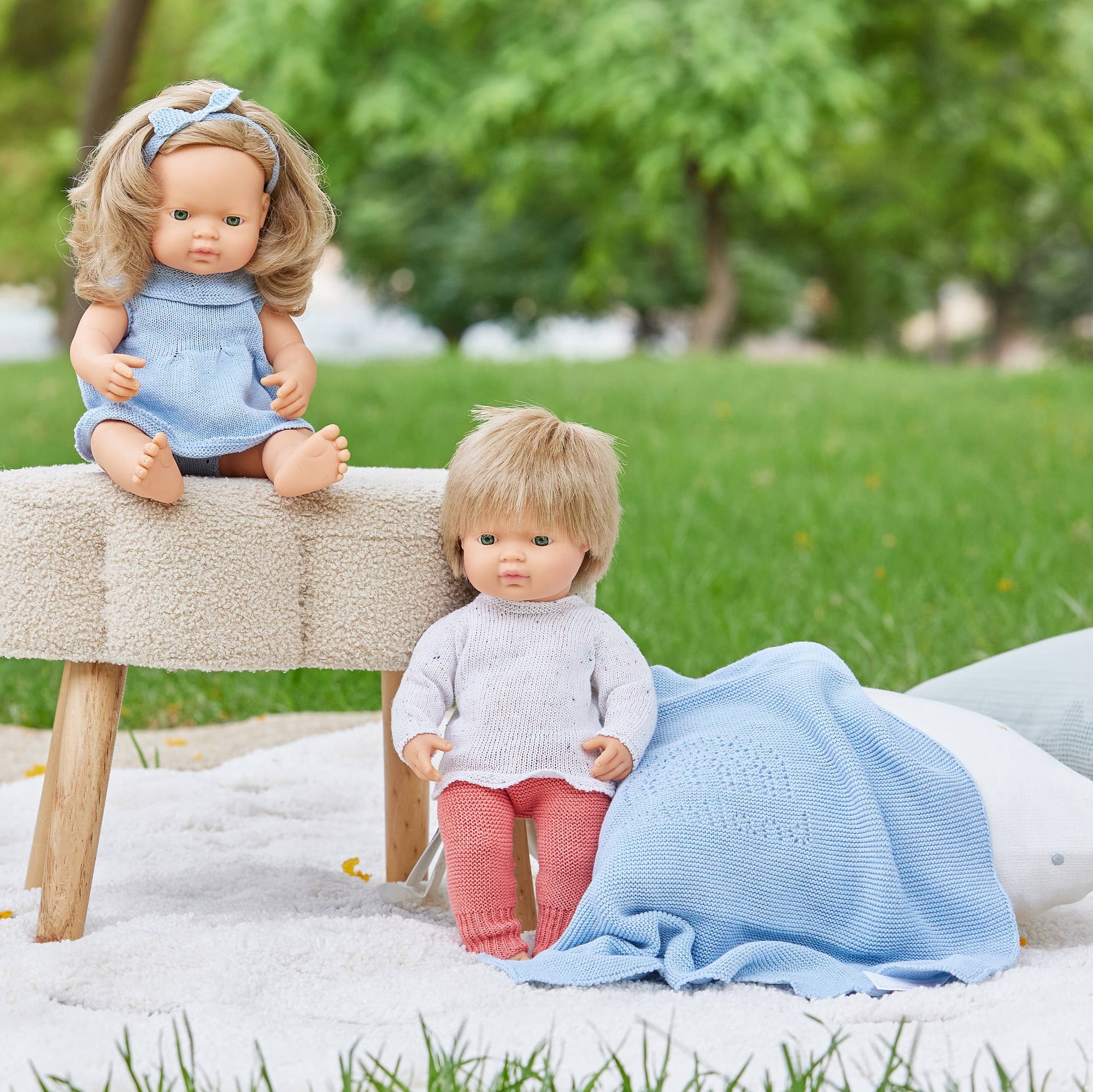 Child holding a baby doll wrapped in a blue blanket outdoors.