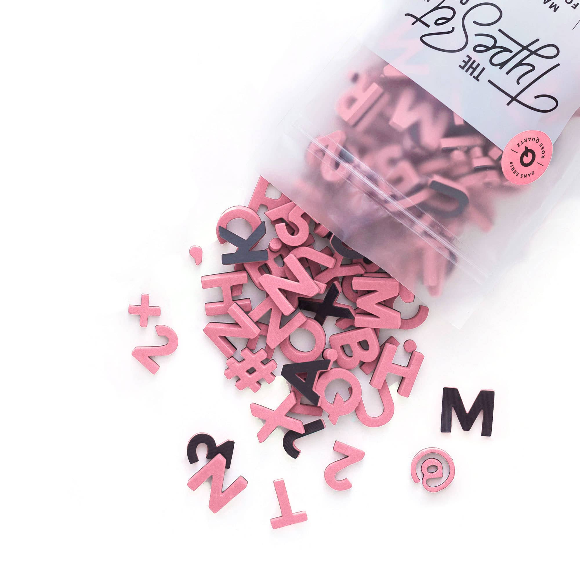 Pink and black letter-shaped confetti spilling out of a clear bag on a white background.
