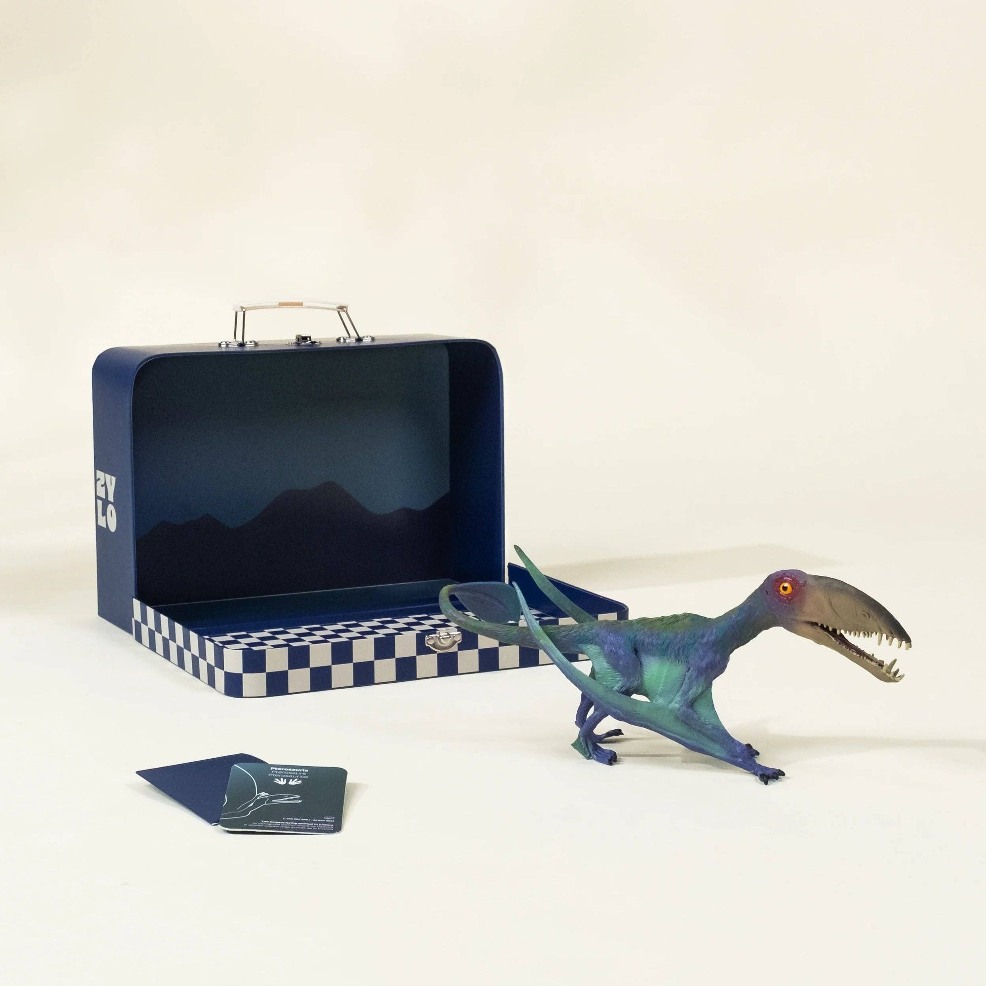 Blue dinosaur toy with checkered base and metallic suitcase on a beige background