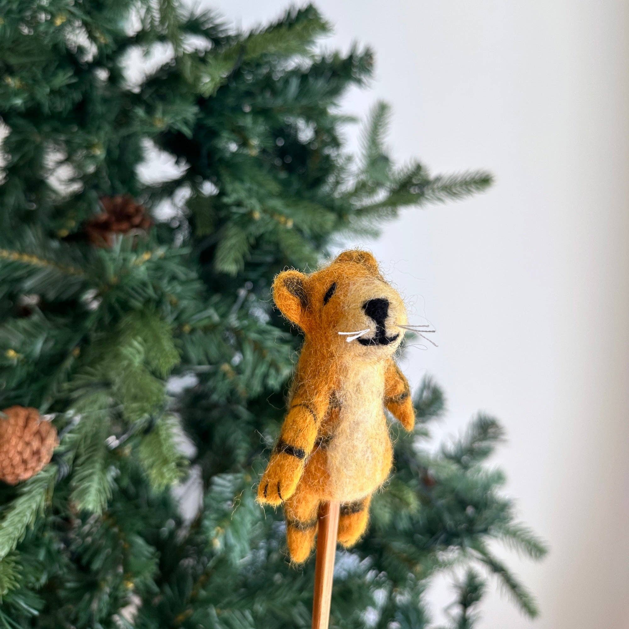 Felted tiger toy on a stick in front of a Christmas tree
