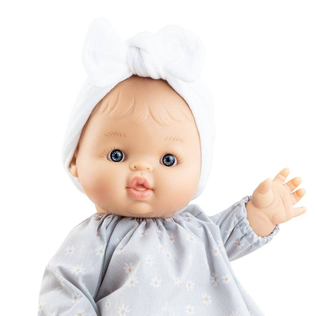 A baby doll with a realistic face, wearing a light blue long-sleeve dress with small white floral patterns, white tights, and a white bonnet with bow details, isolated on a white background.