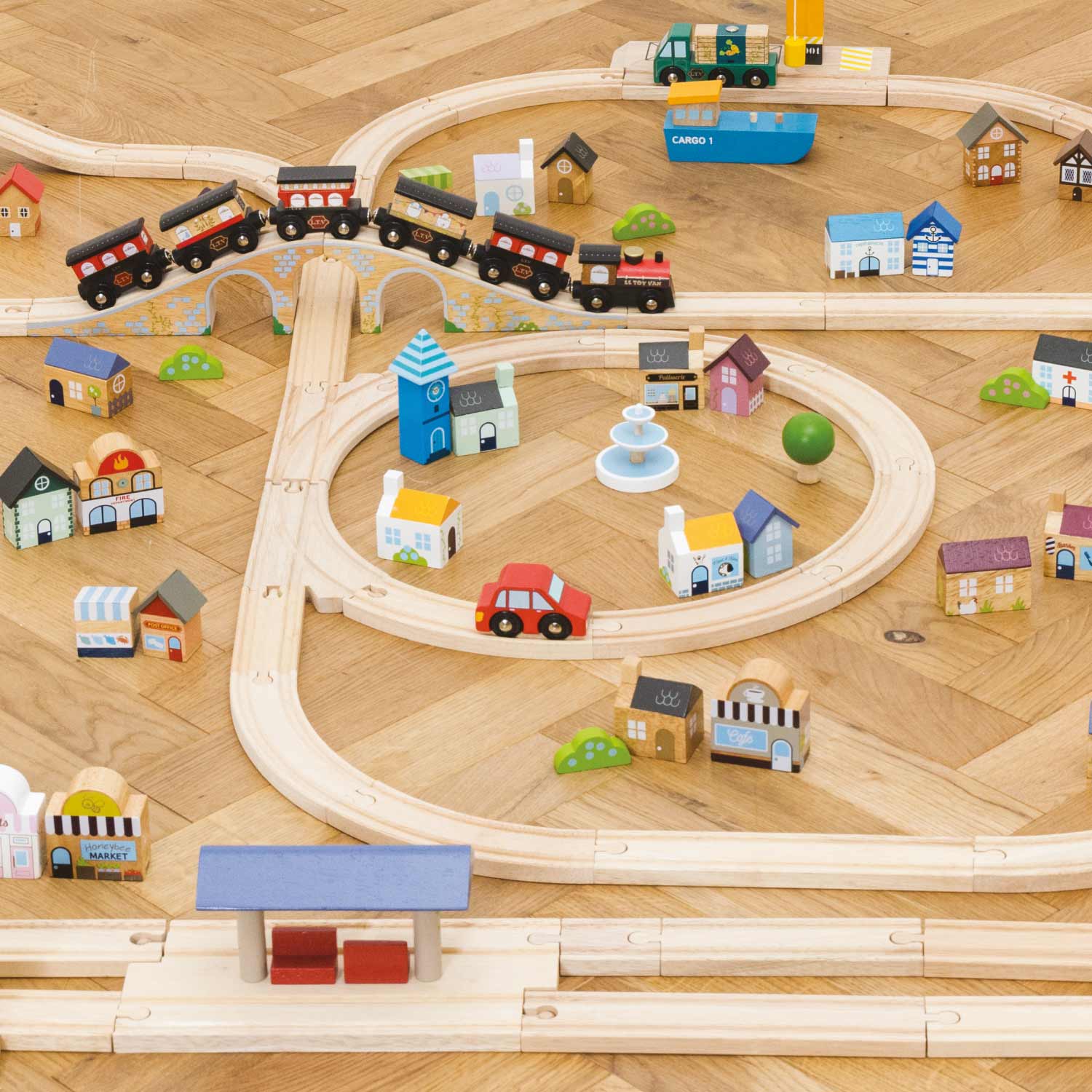 Wooden toy train set with tracks, trains, and buildings on a wooden surface