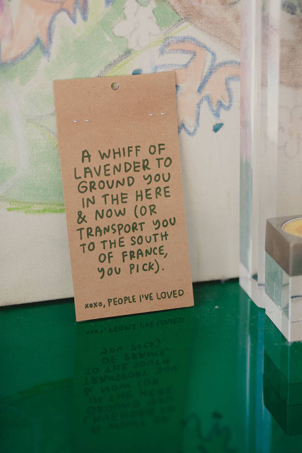 Handwritten tag on a green surface with text about lavender and a candle in the background.