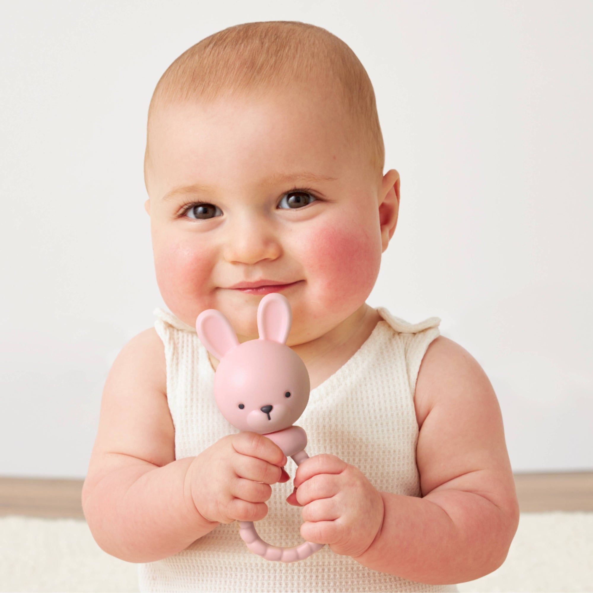 Baby holding a pink bunny toy against a white background