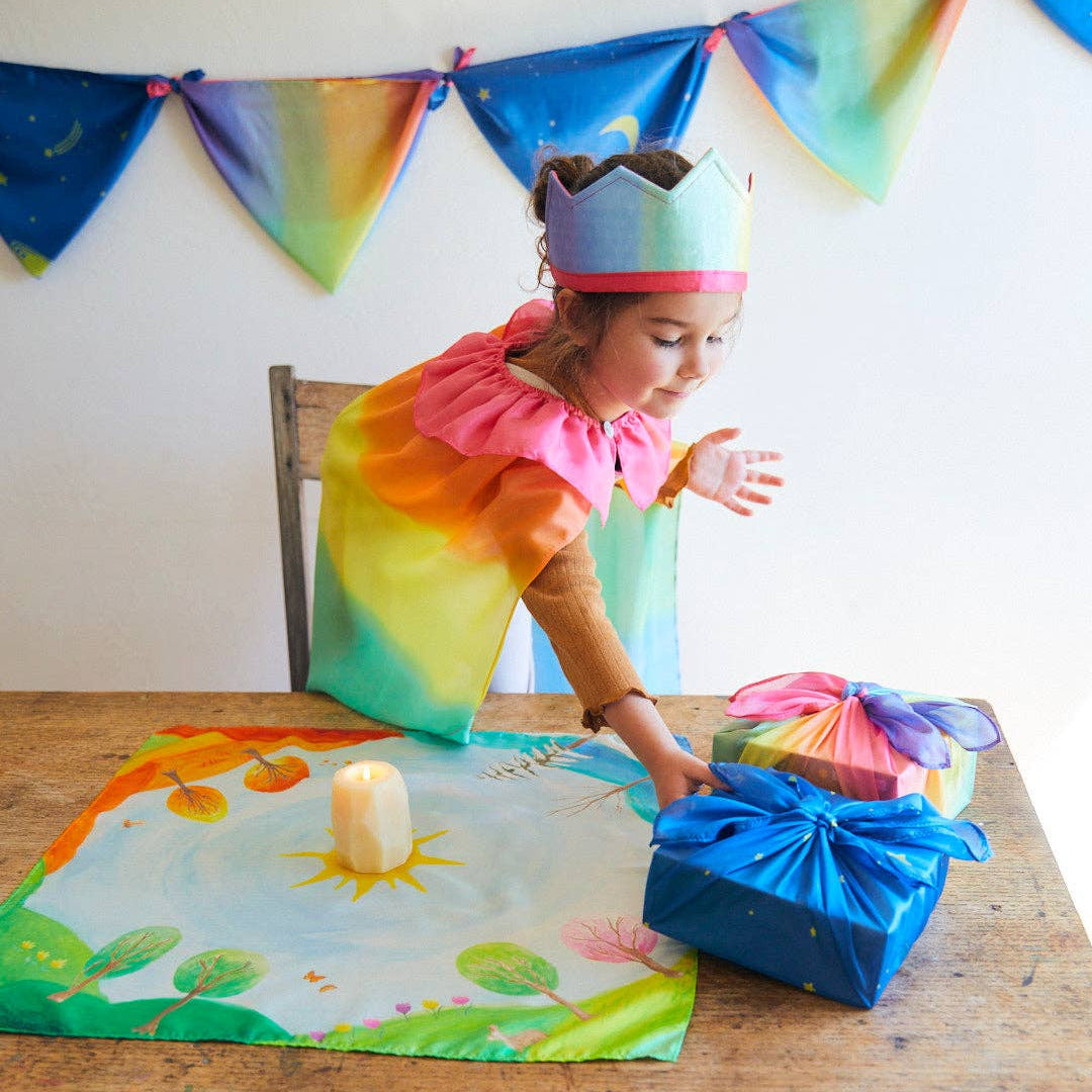 Child in colorful costume opening a gift at a table with a decorated tablecloth.