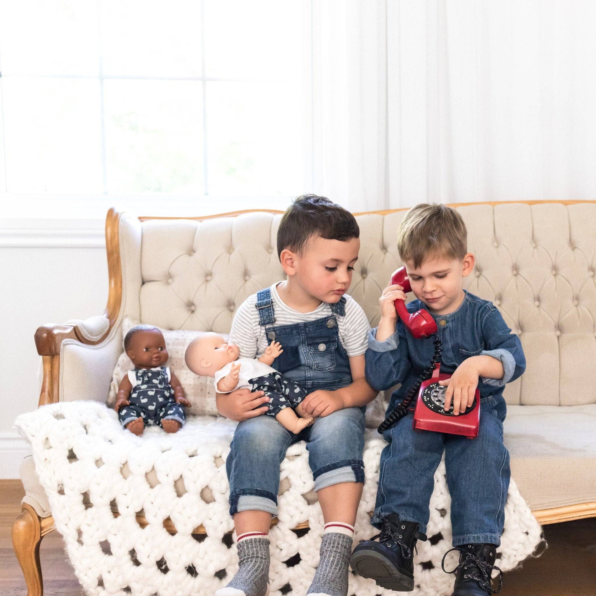 Two children sitting on a couch with dolls and a toy phone.