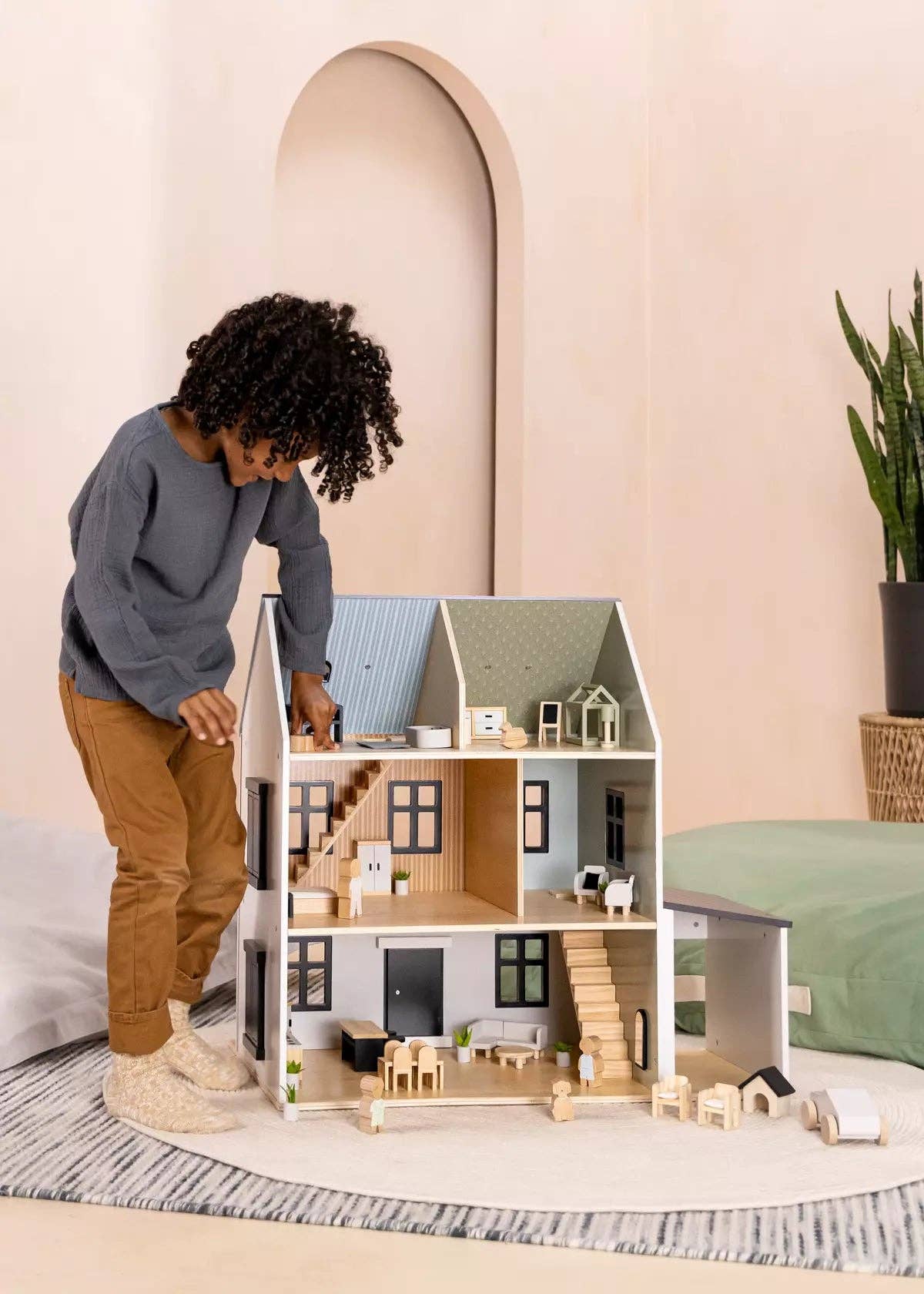 Child playing with a dollhouse in a room with a pink wall and a plant.