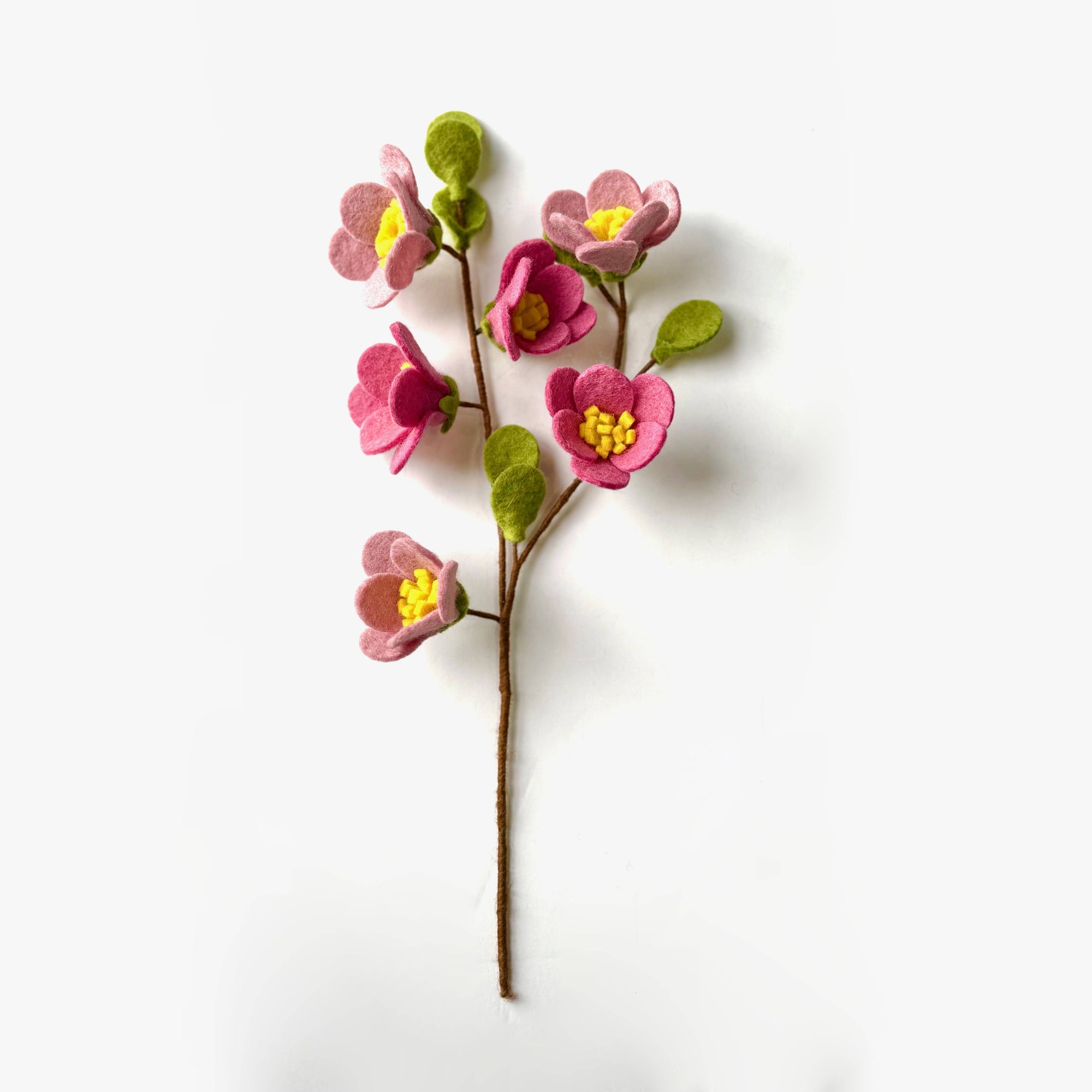 Artificial flower branch with pink flowers and green leaves on a white background