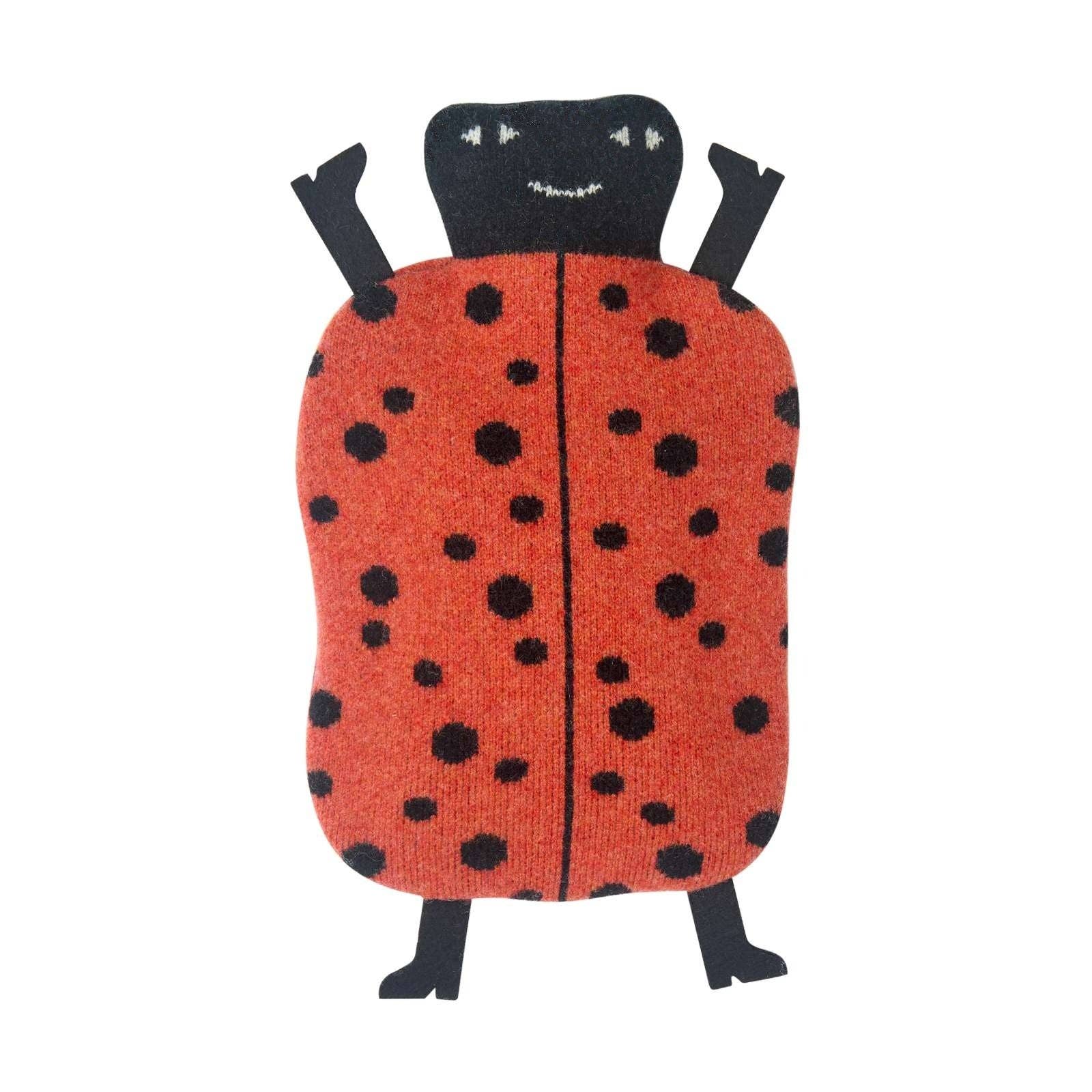 A knitted ladybug-shaped cushion or pillow with a red-orange body, black spots, and a black head with embroidered facial details, shown on a plain white background.