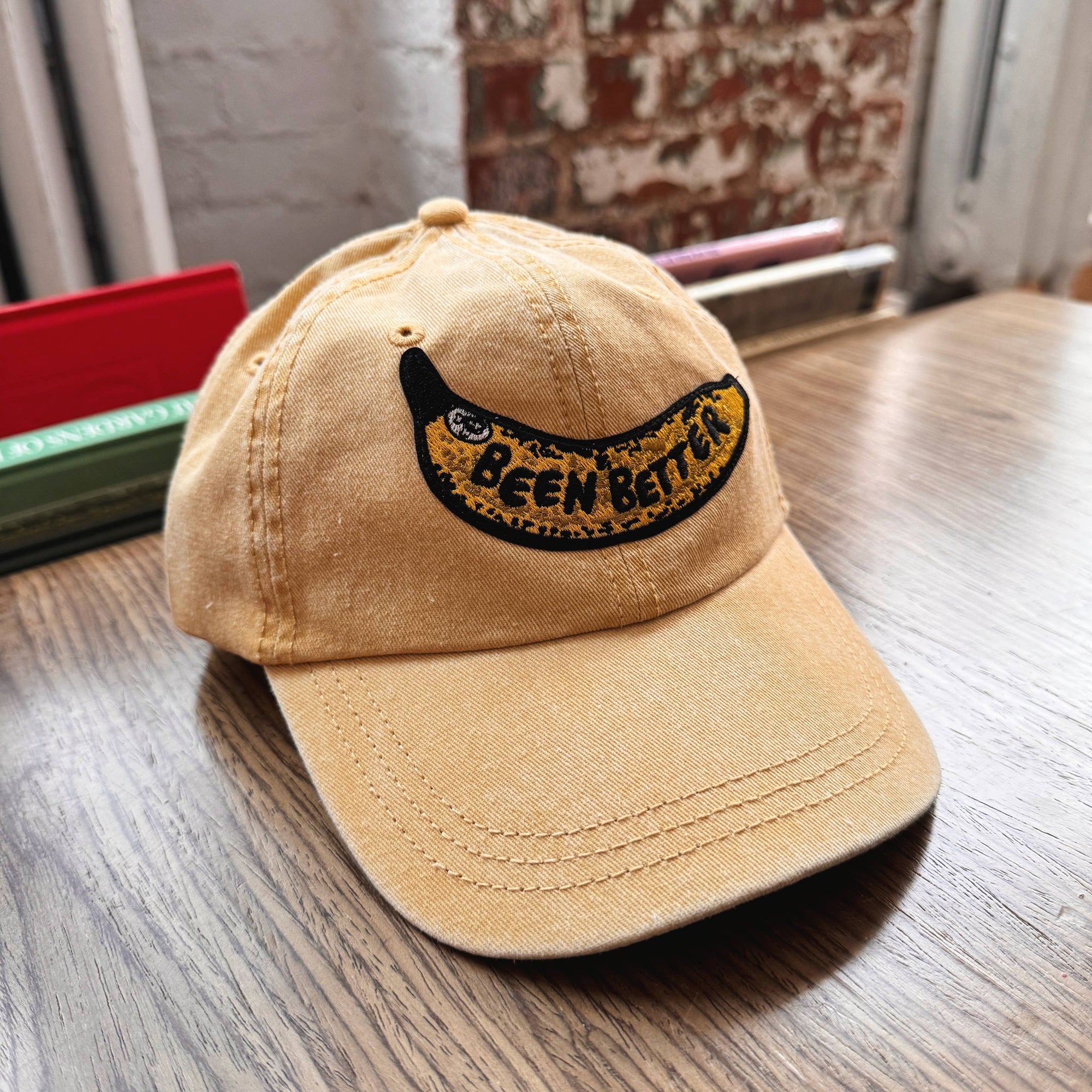 Beige cap with 'Been There' embroidery on a wooden surface