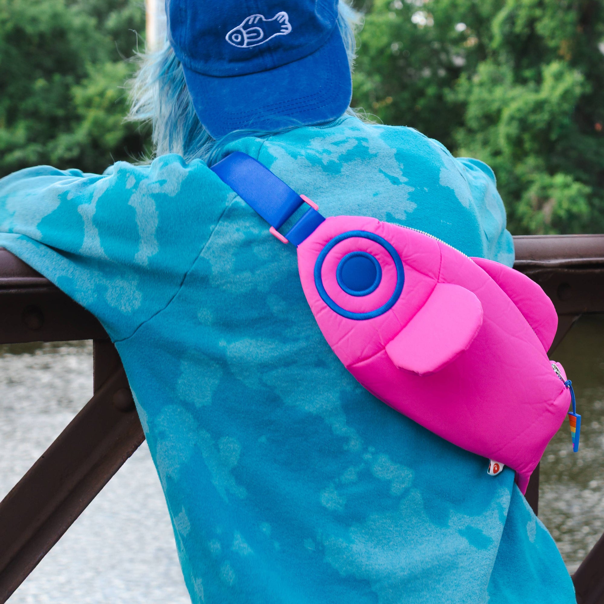 Person wearing a blue cap and turquoise jacket with a pink and blue fanny pack.