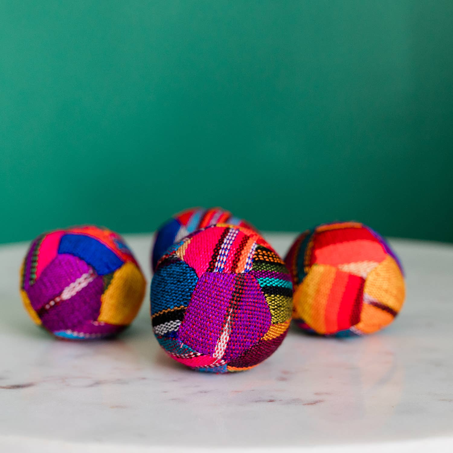 Four colorful fabric balls on a marble surface with a green background
