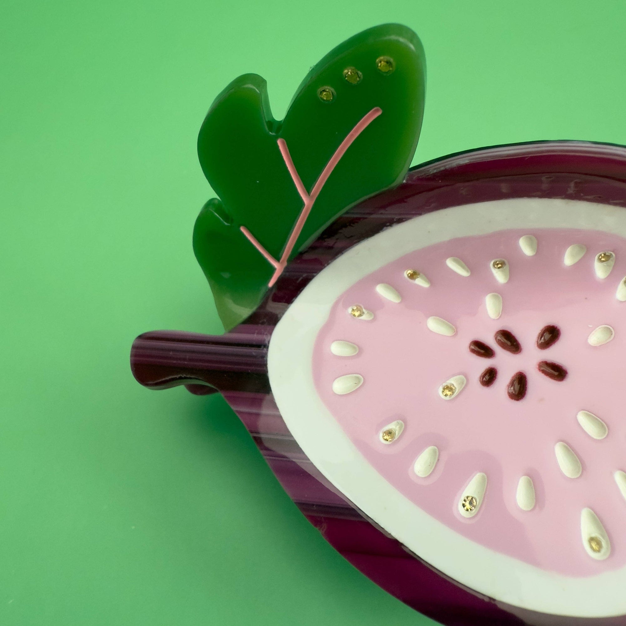 Sliced dragon fruit hair clip with pink flesh and green rind on a green background