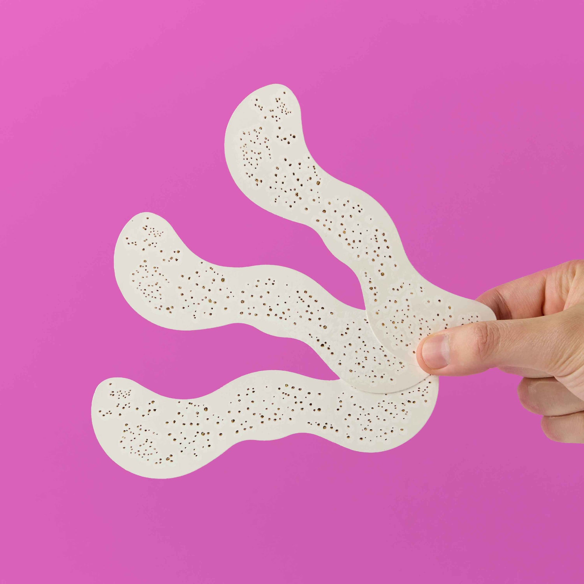 Hand holding a white textured mat against a pink background