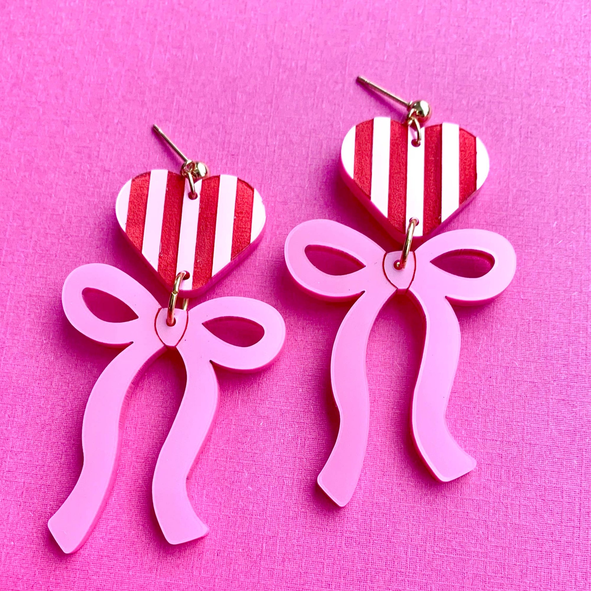 Heart-shaped earrings with pink bows on a pink background