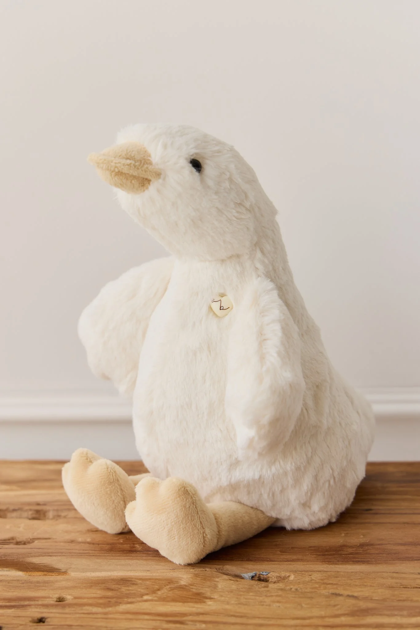 White plush duck toy on a wooden surface with a plain background