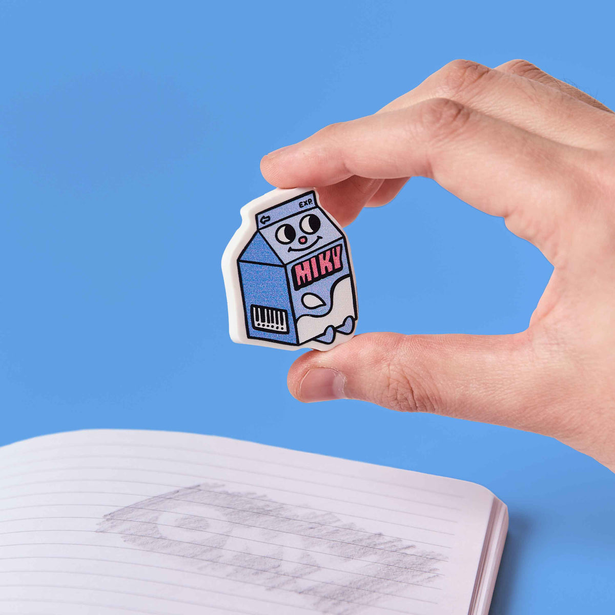 Hand holding a cartoon milk carton character sticker with a blue background