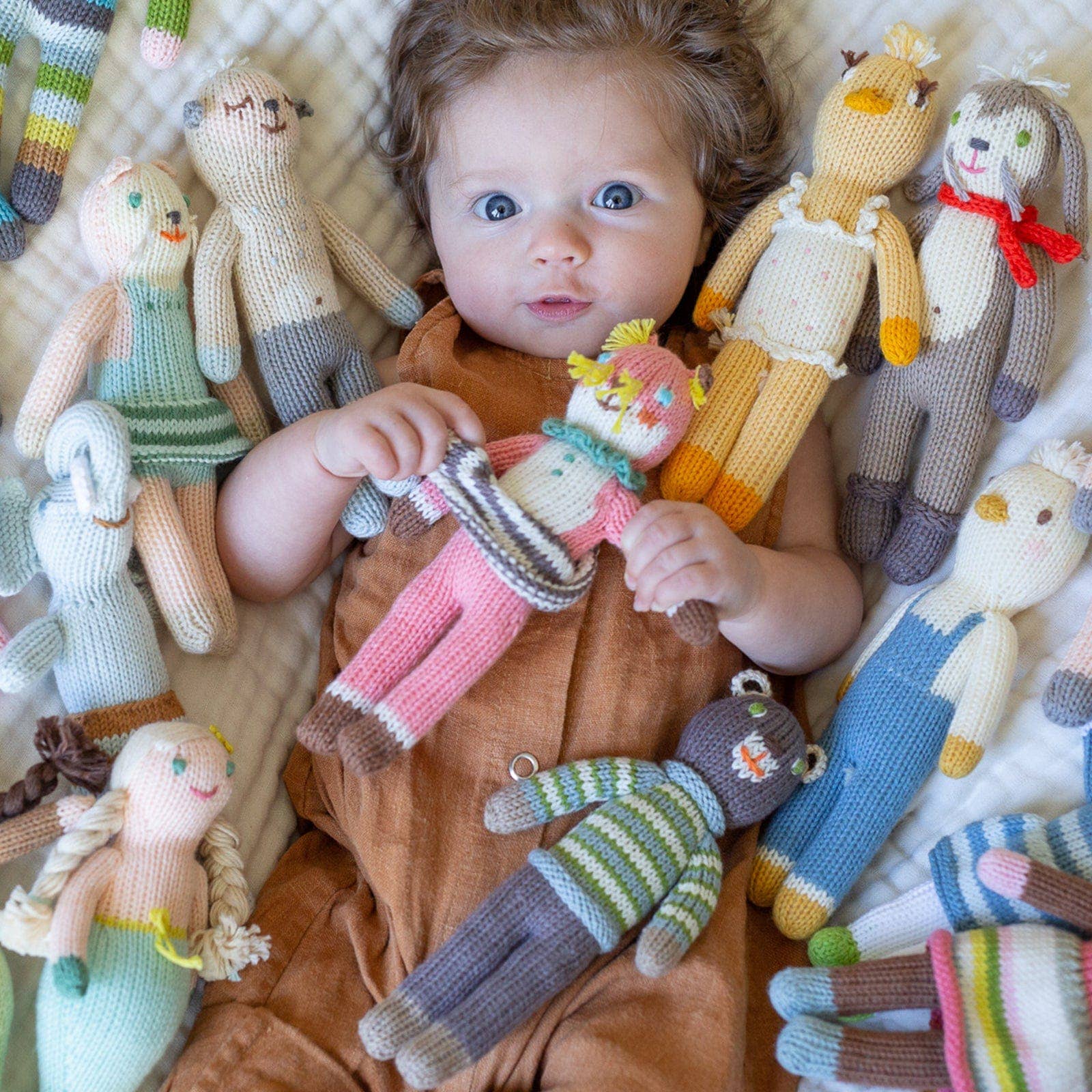 Baby surrounded by hand-knitted dolls on a textured surface