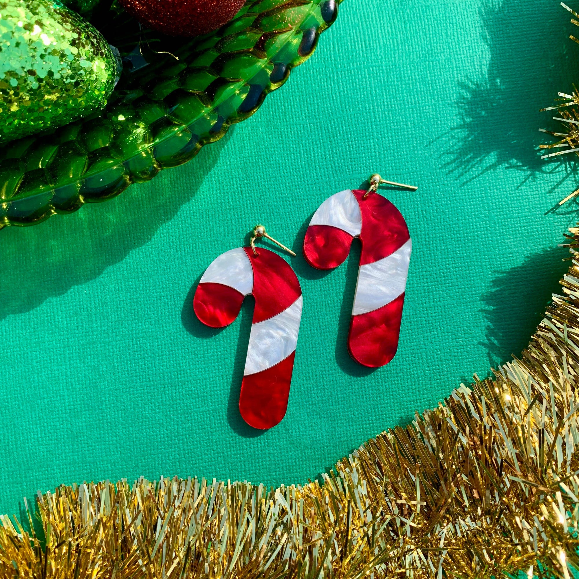 Candy cane-shaped earrings on a green background with festive decorations