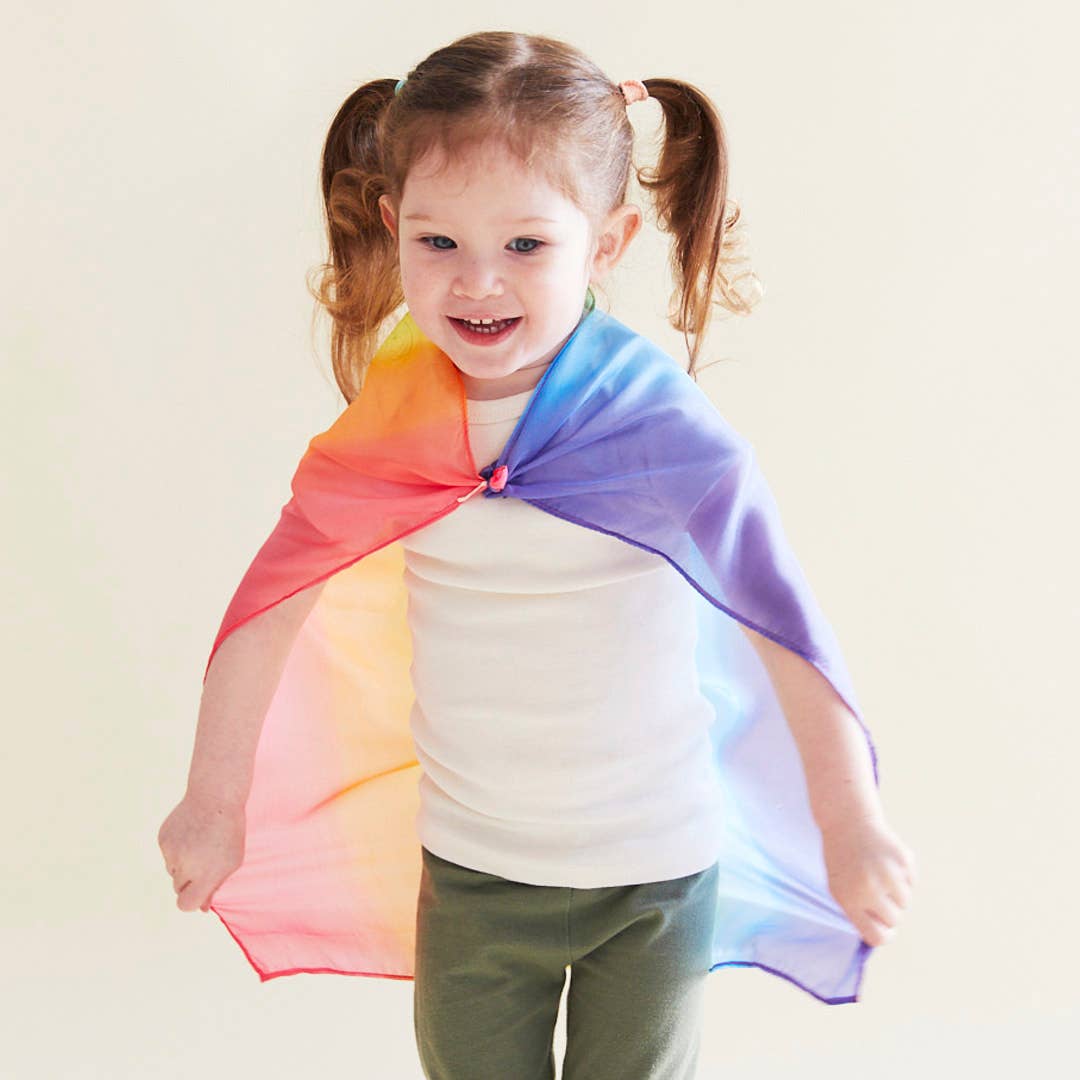 Child wearing a rainbow-colored cape against a plain background