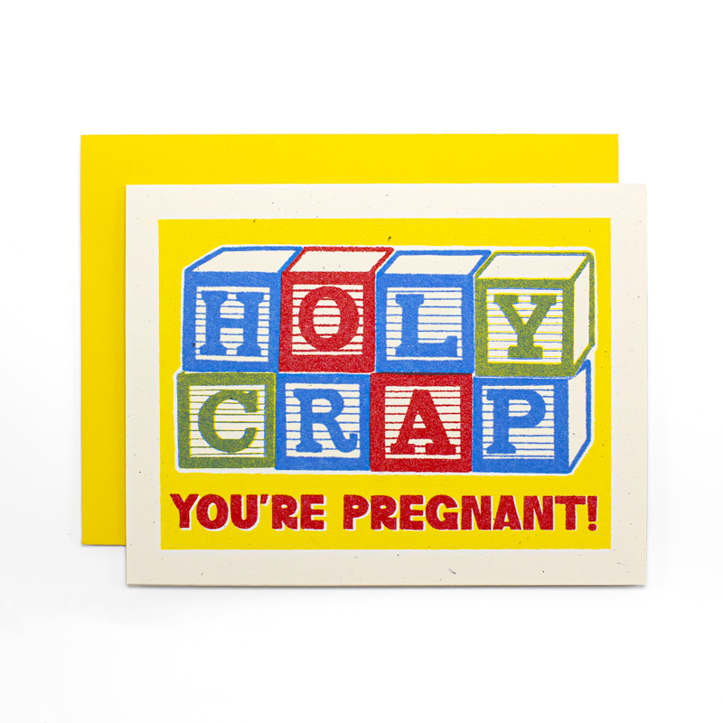 A novelty greeting card with a bright yellow envelope behind it. The card has a white border and features colorful toy block letters spelling 'HOLY CRAP' above the red text 'YOU'RE PREGNANT!'.