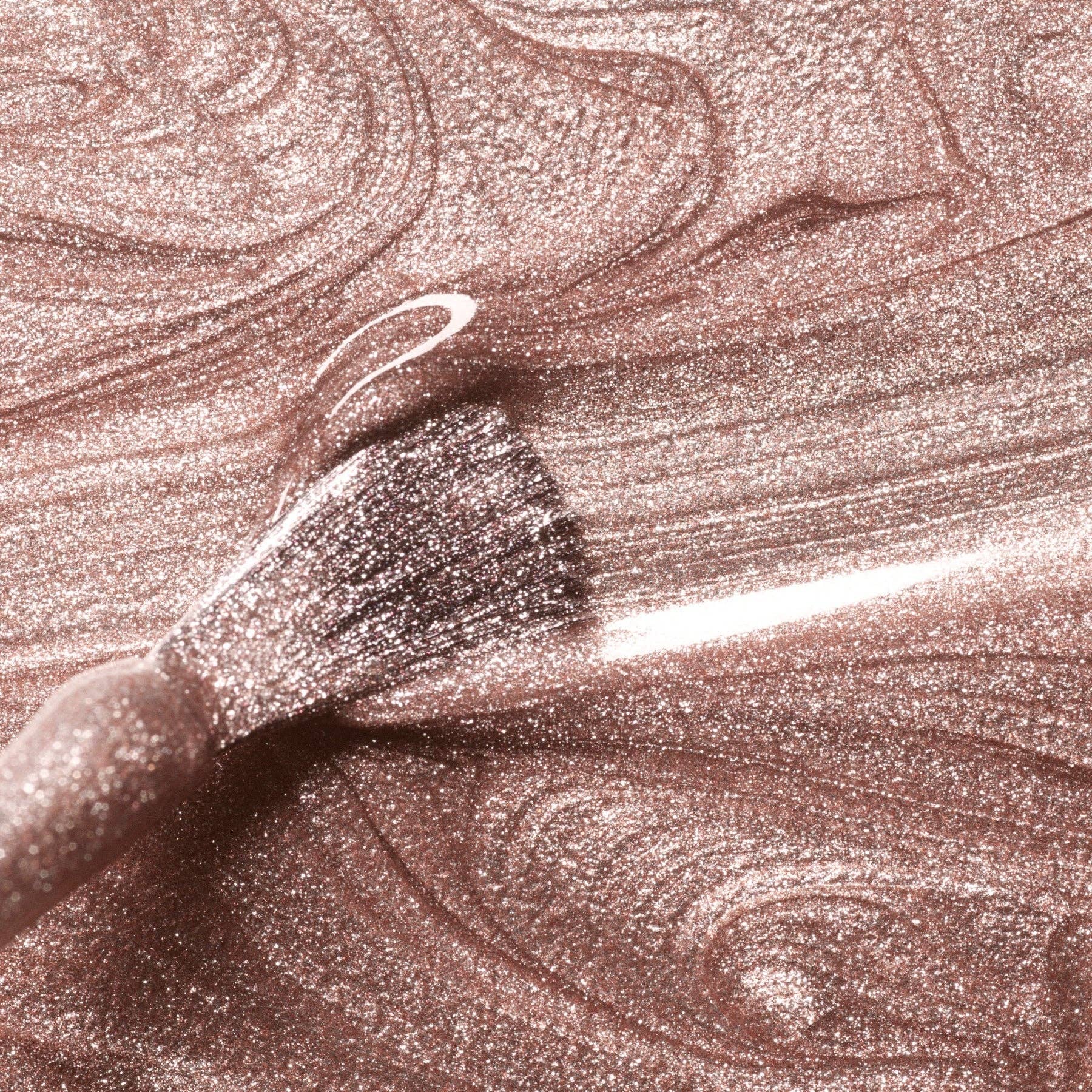 Close-up of a makeup brush with glittery pink cream on a matching background