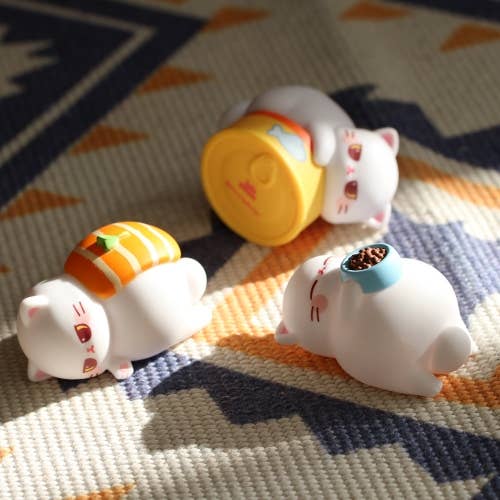 Three small white cat figurines with colorful accessories on a patterned fabric background