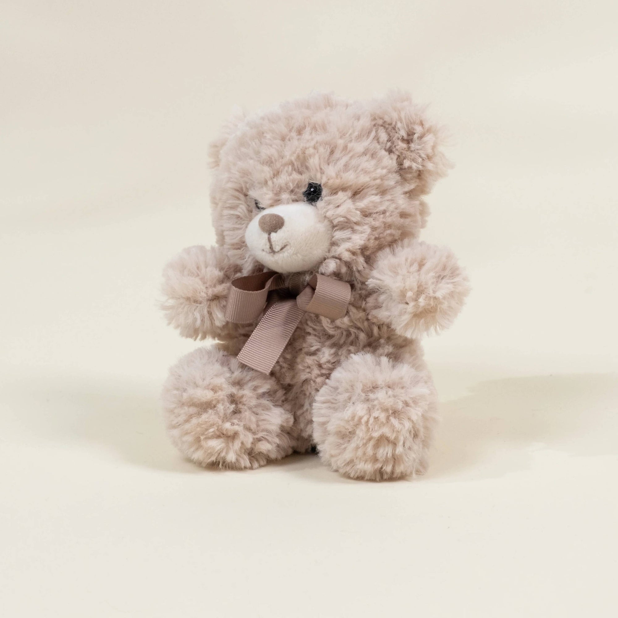 Plush teddy bear with a pink bow on a light beige background