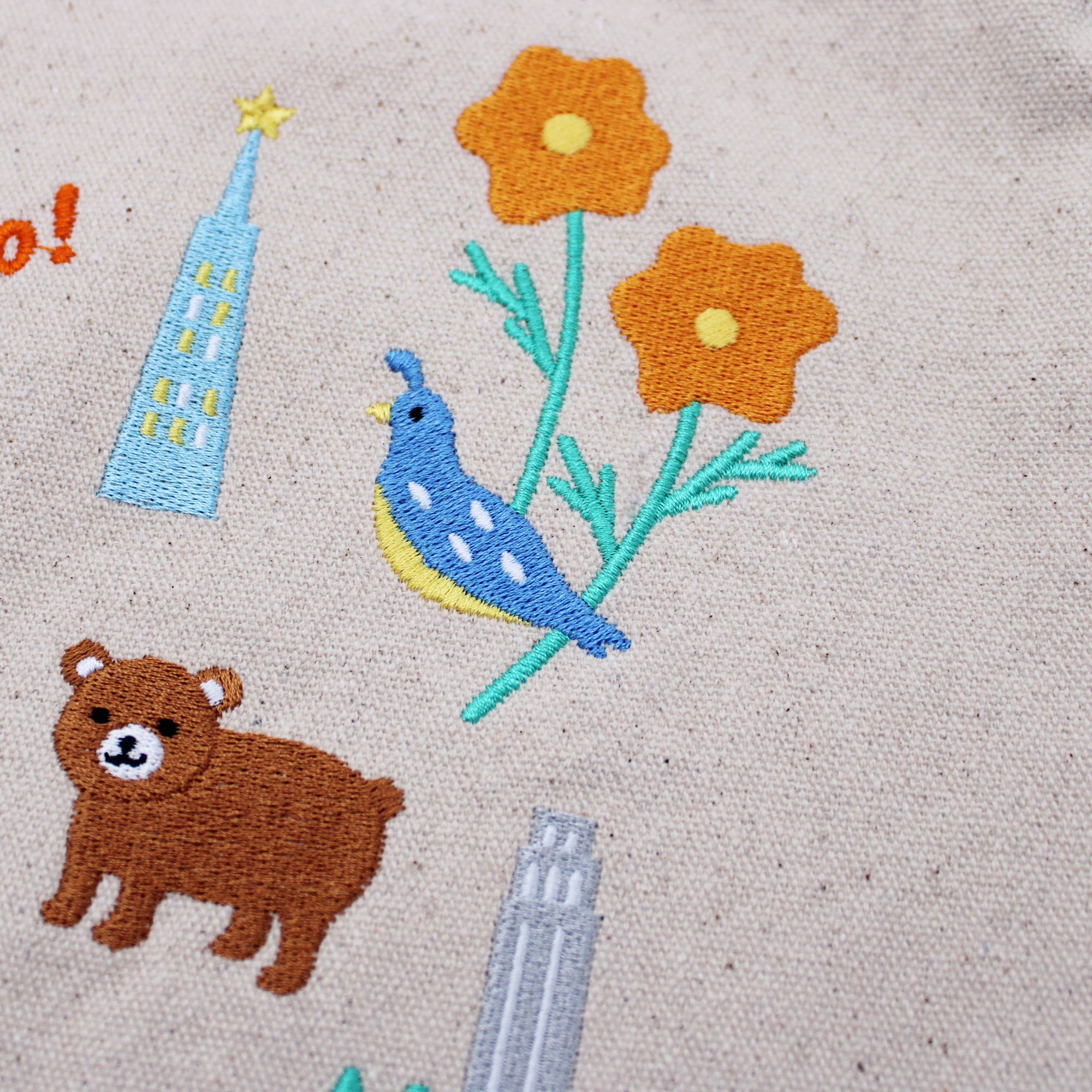 Embroidered design on fabric featuring a bear, flowers, and buildings.