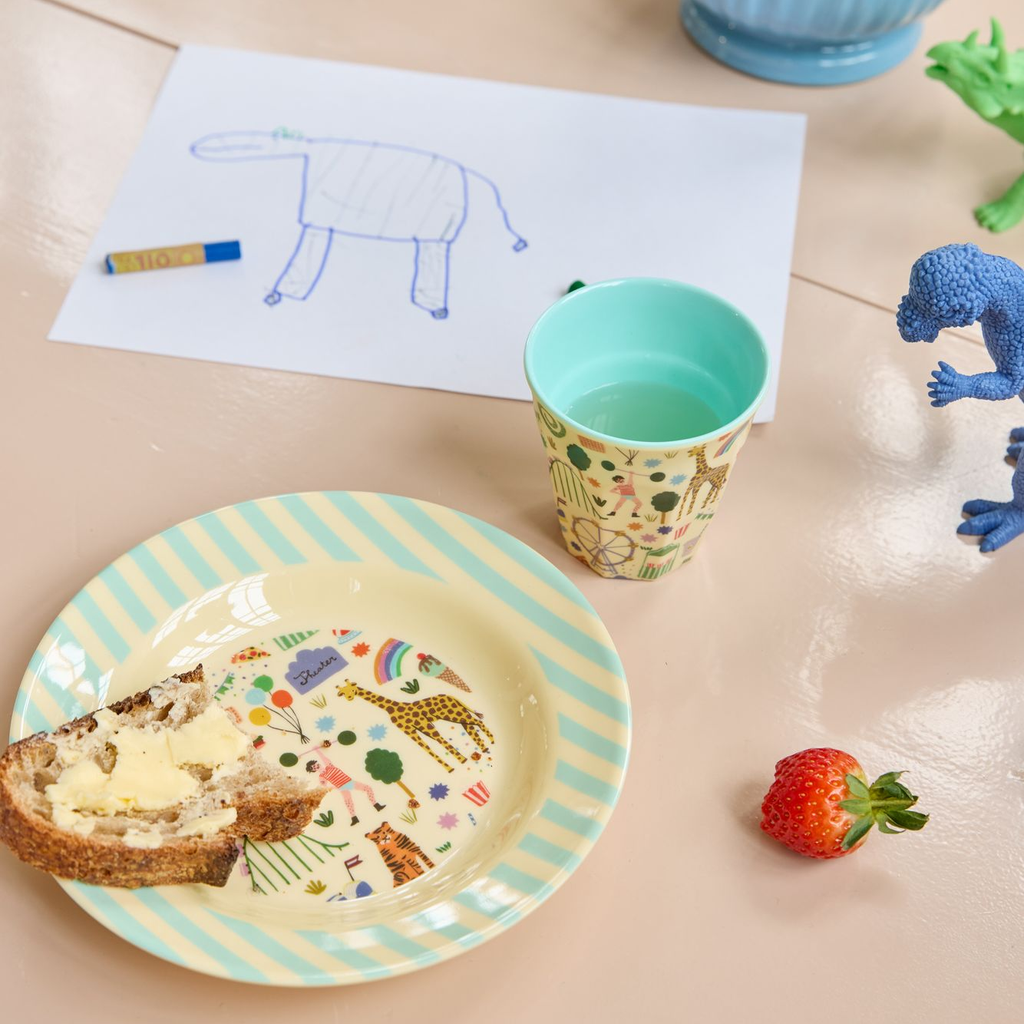 Children's table setting with plate, cup, and toys on a light surface.