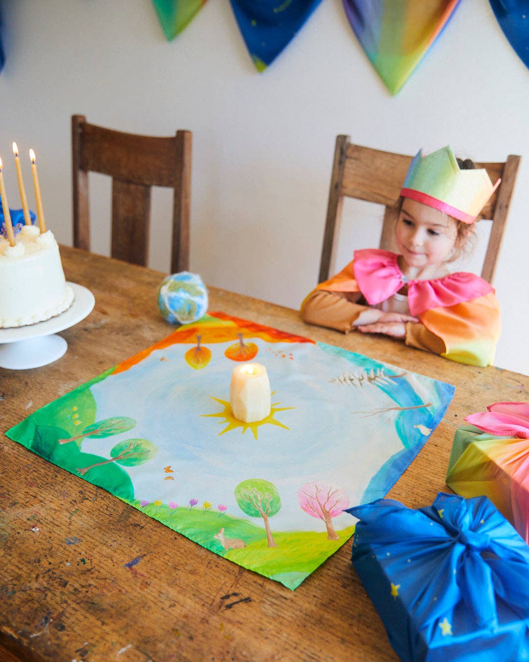 Child at a birthday party with a decorated table, cake, and balloons.