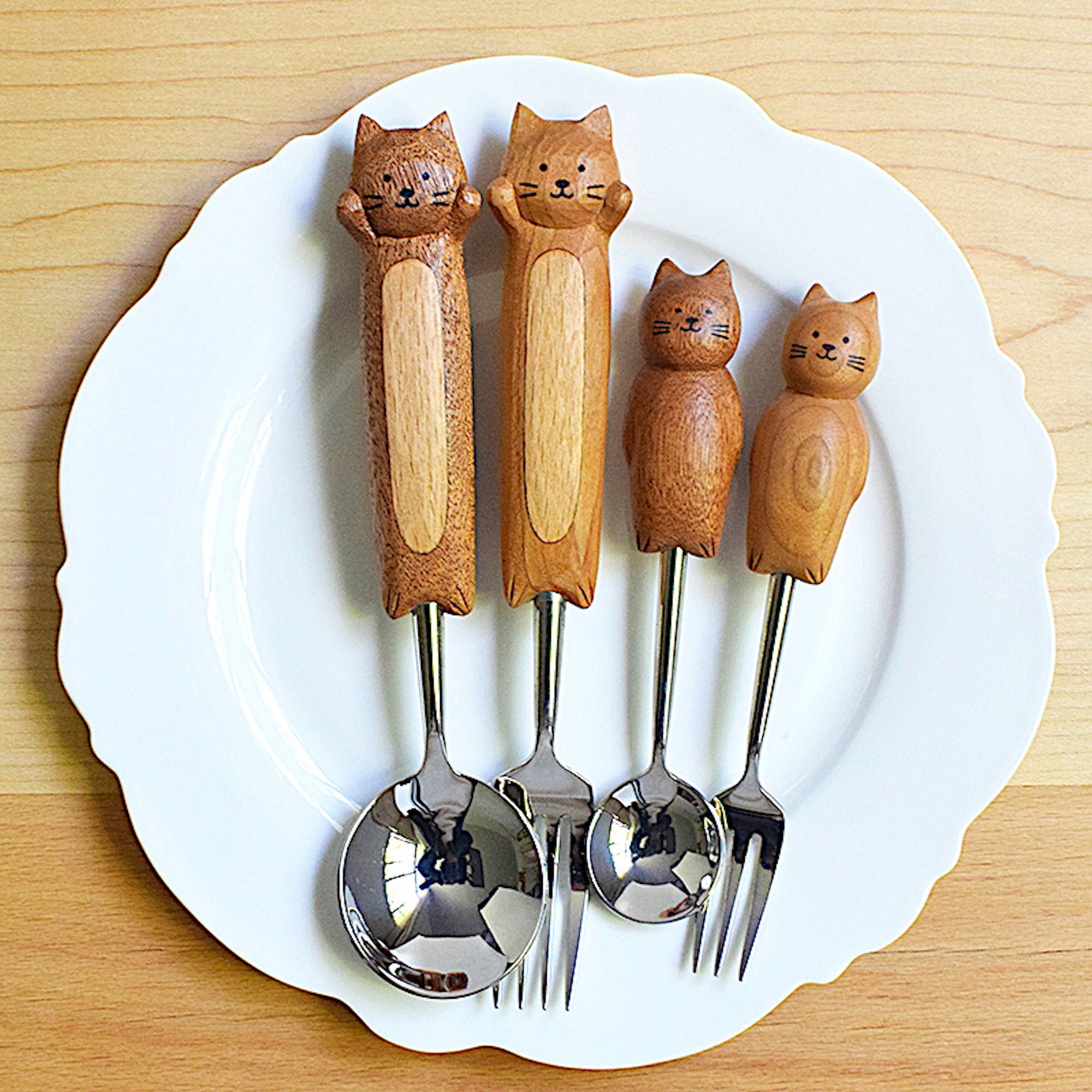 Four wooden-handled cutlery sets shaped like cats on a white plate.