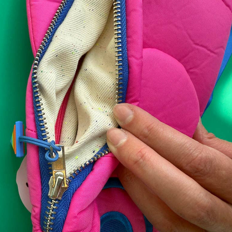 Hand opening a pink bag with a blue zipper on a green background