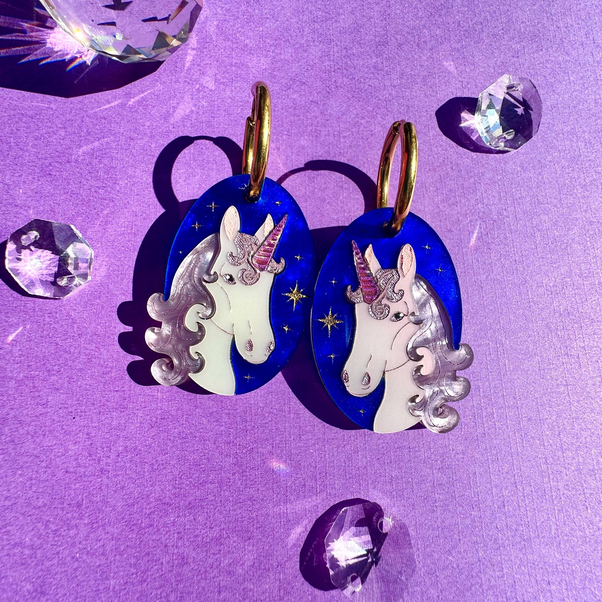 Unicorn-shaped earrings on a purple background with crystals