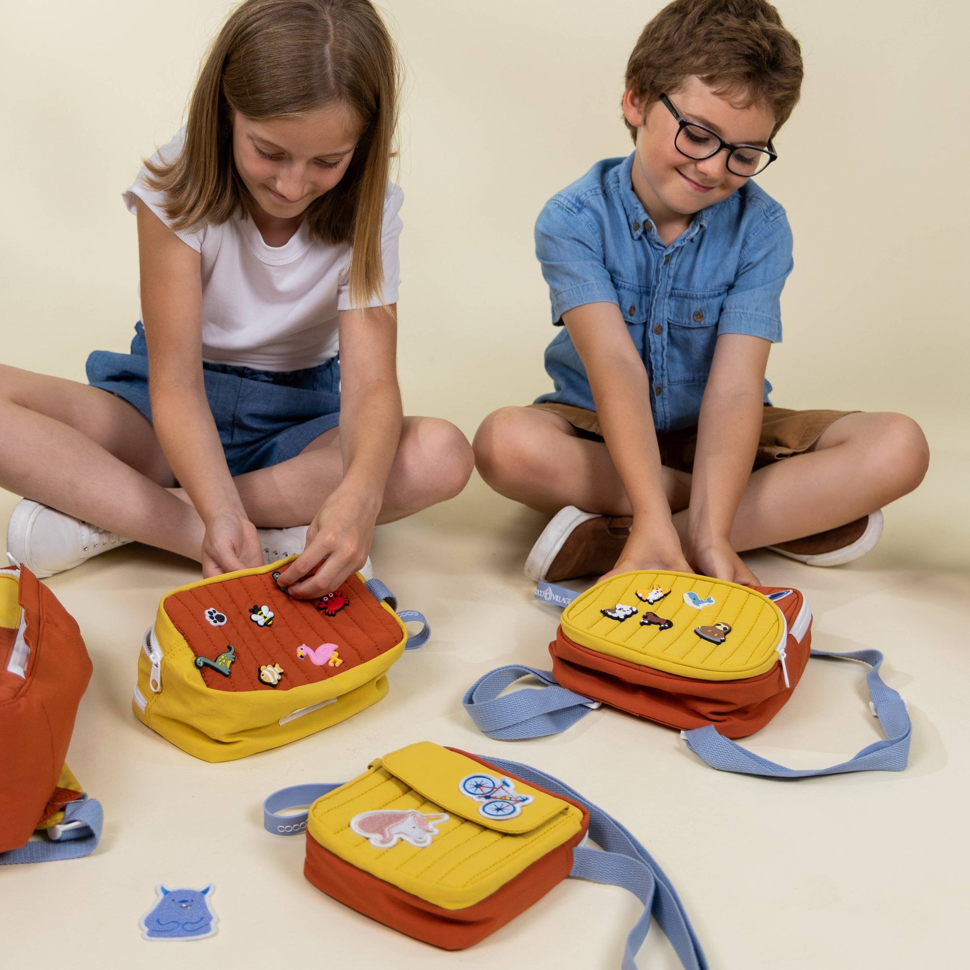Two children playing with colorful bags on a beige floor.