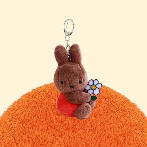 Plush bunny keychain with a flower on an orange surface