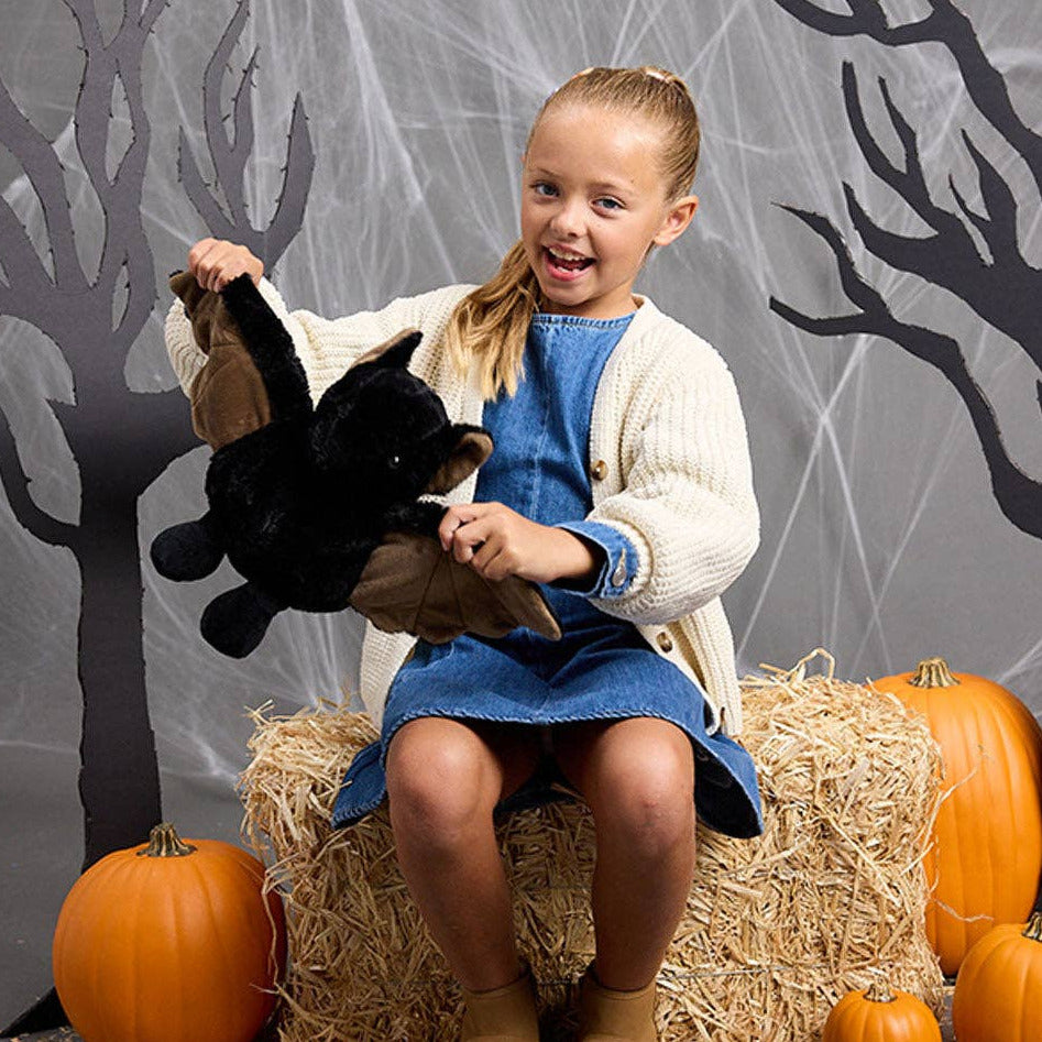 Child holding a stuffed animal in front of a Halloween-themed backdrop with pumpkins and hay.