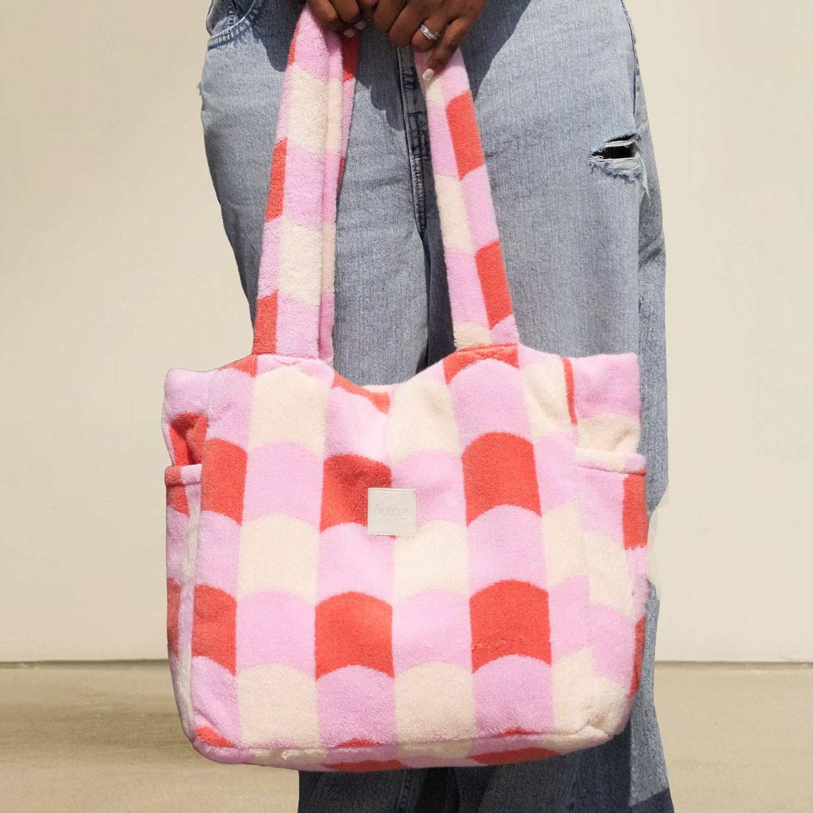 Person holding a pink and red checkered bag against a neutral background
