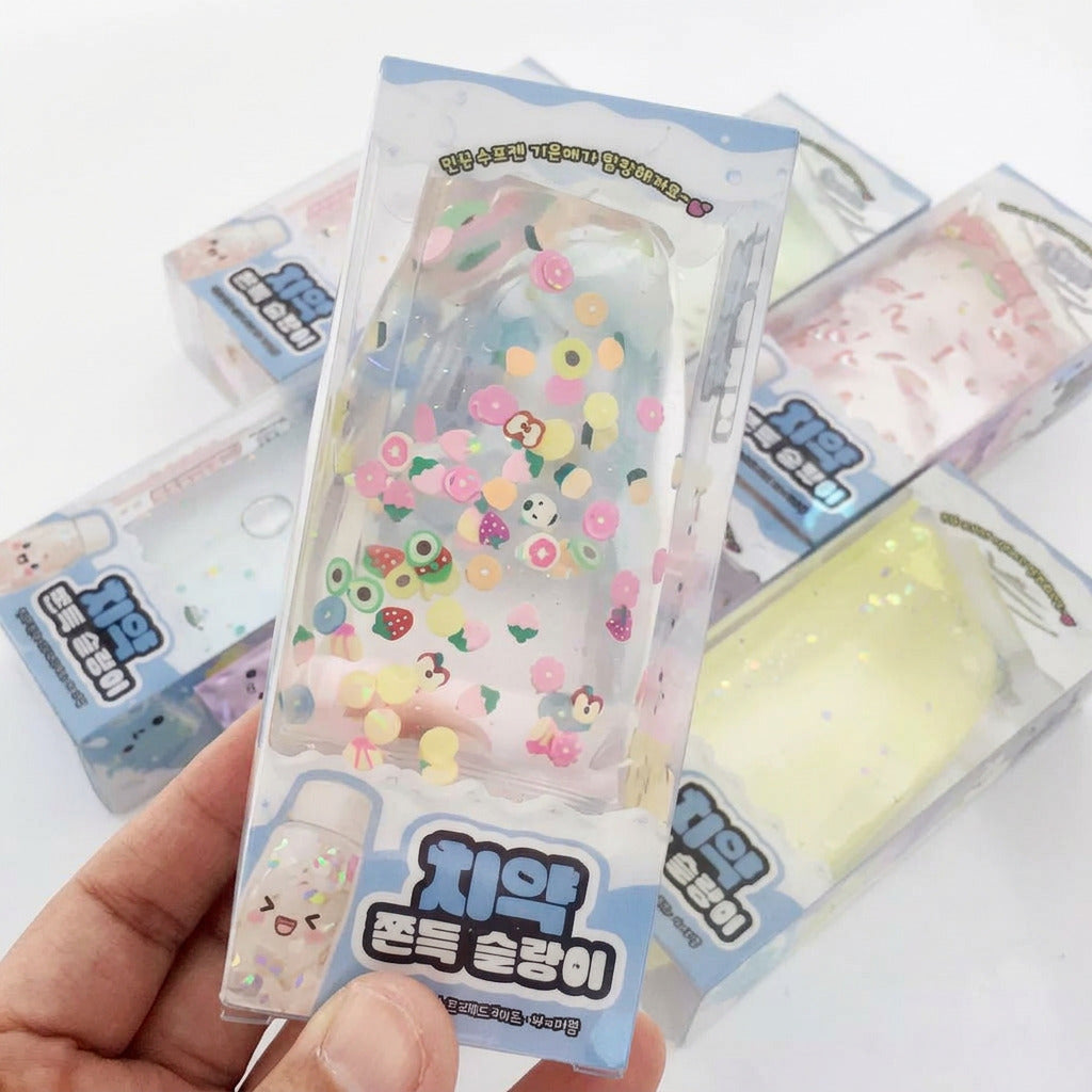 A hand holds a packaged clear phone case decorated with colorful cartoon characters, flowers, and small charms. Several similar packaged cases are fanned out in the background on a white surface.