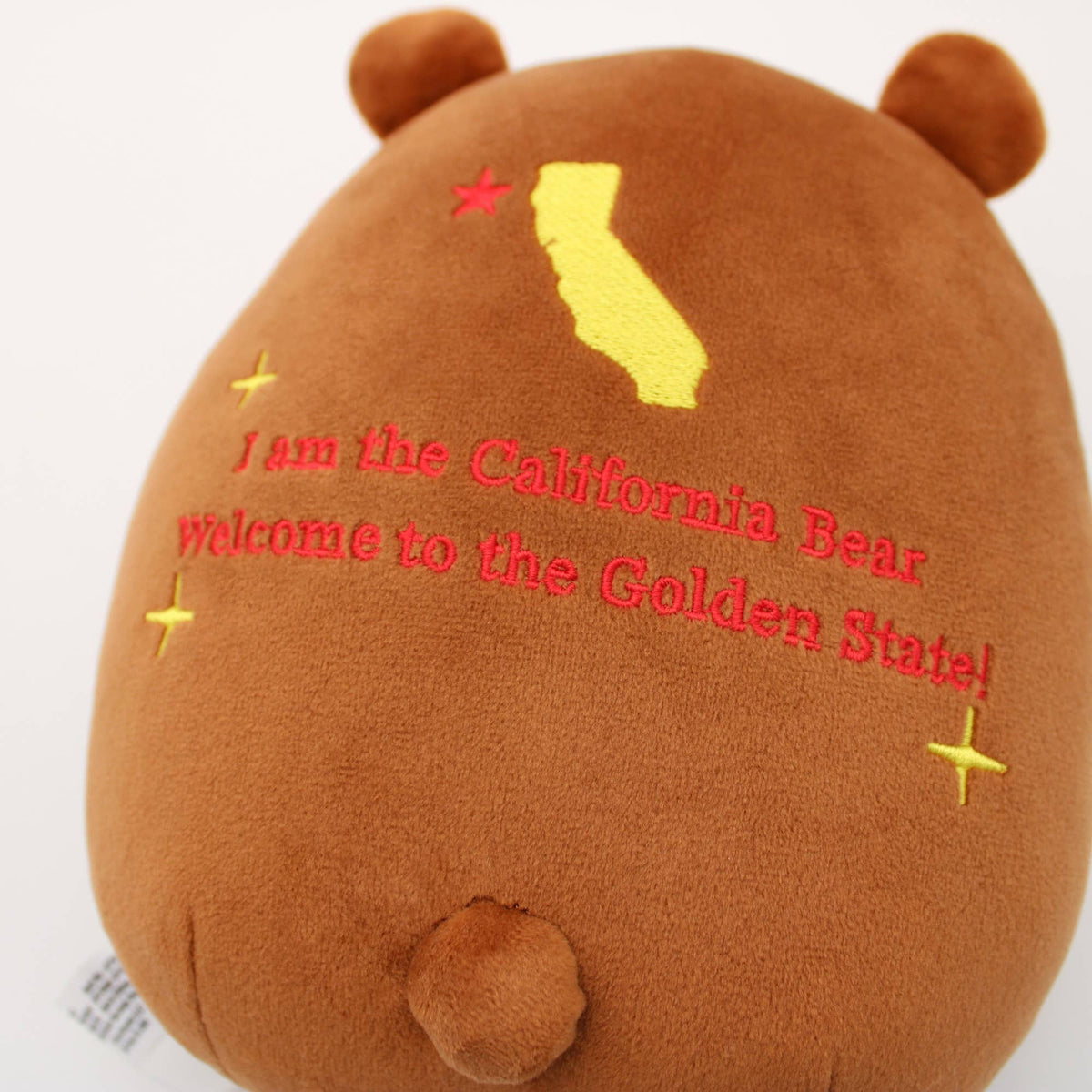A brown plush bear toy with embroidered red text reading 'I am the California Bear welcome to the Golden State!' and a yellow California state silhouette on the front, shown against a plain white background.