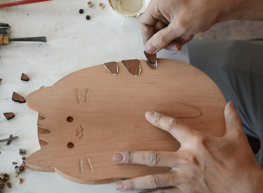 Wooden craft project with hands using tools on a white surface