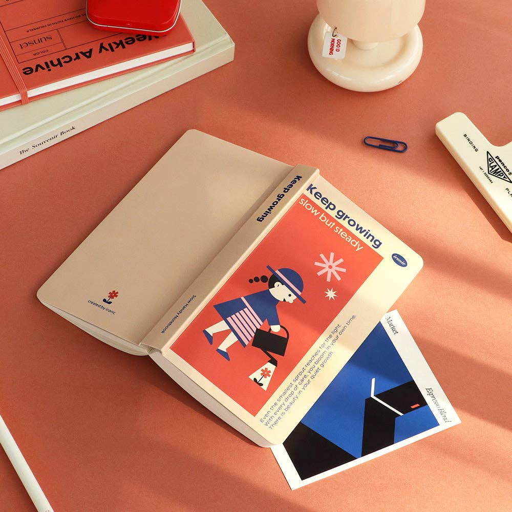 Open notebook with a postcard on a pink surface
