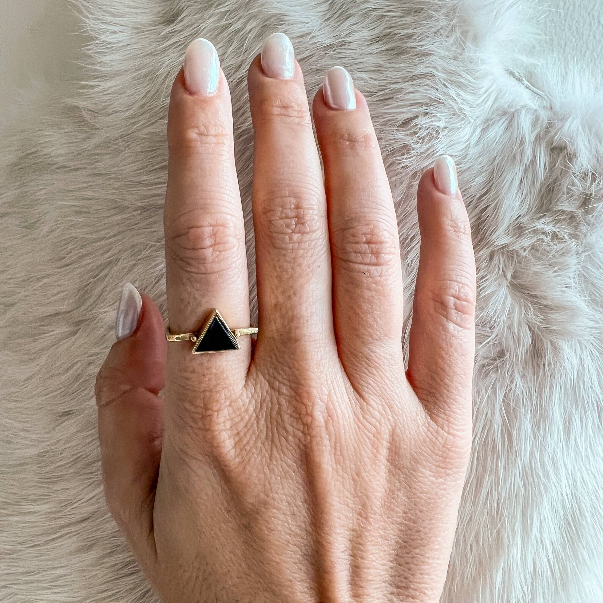 Hand wearing a gold ring with a black triangle on a fur background