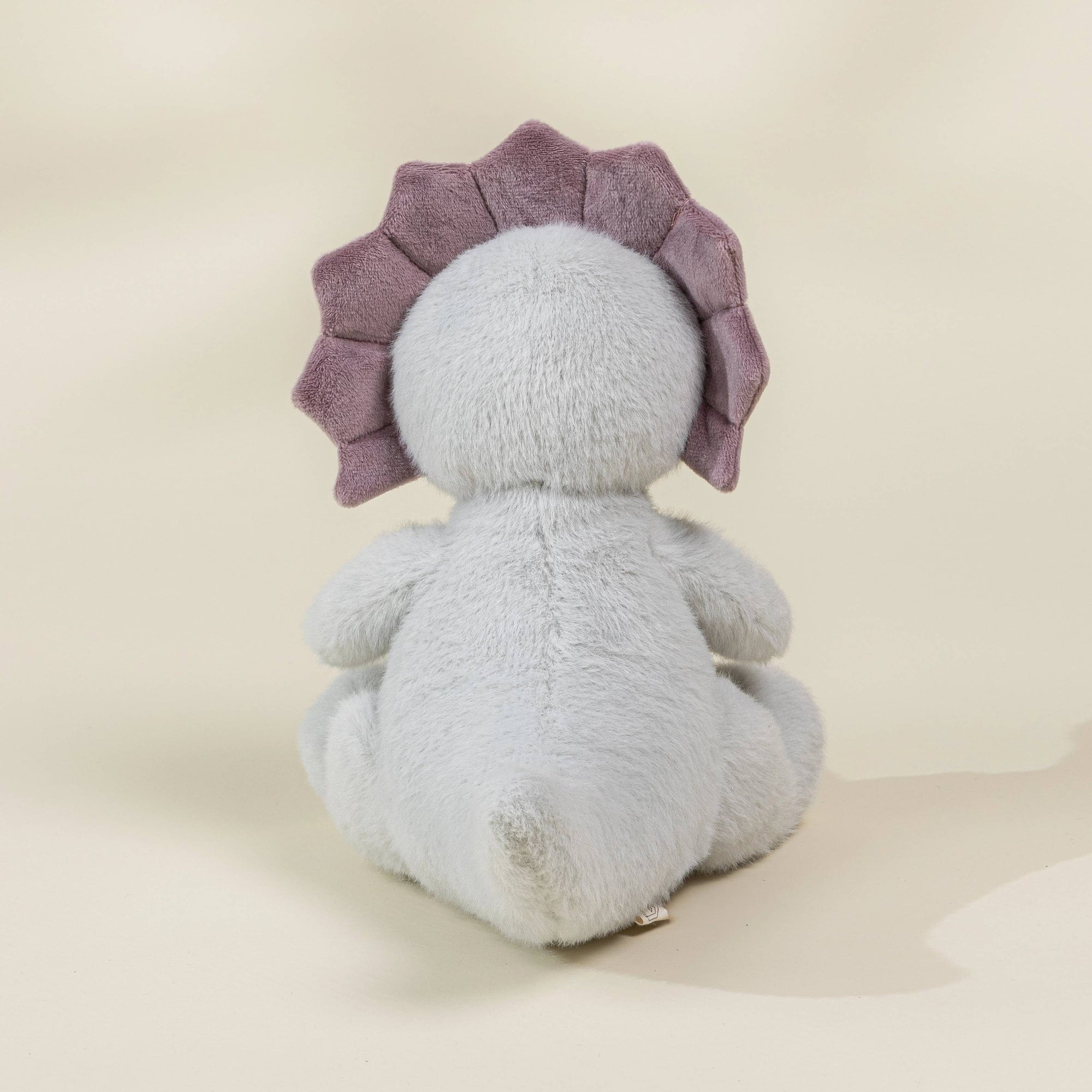Gray plush dino with a purple frill on a beige backgroundl