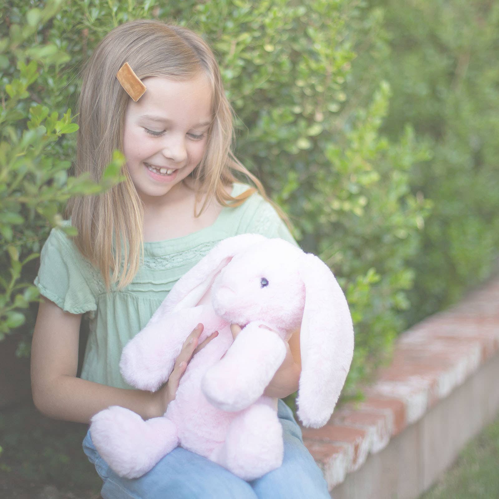 Young girl holding a pink stuffed bunny in a garden setting