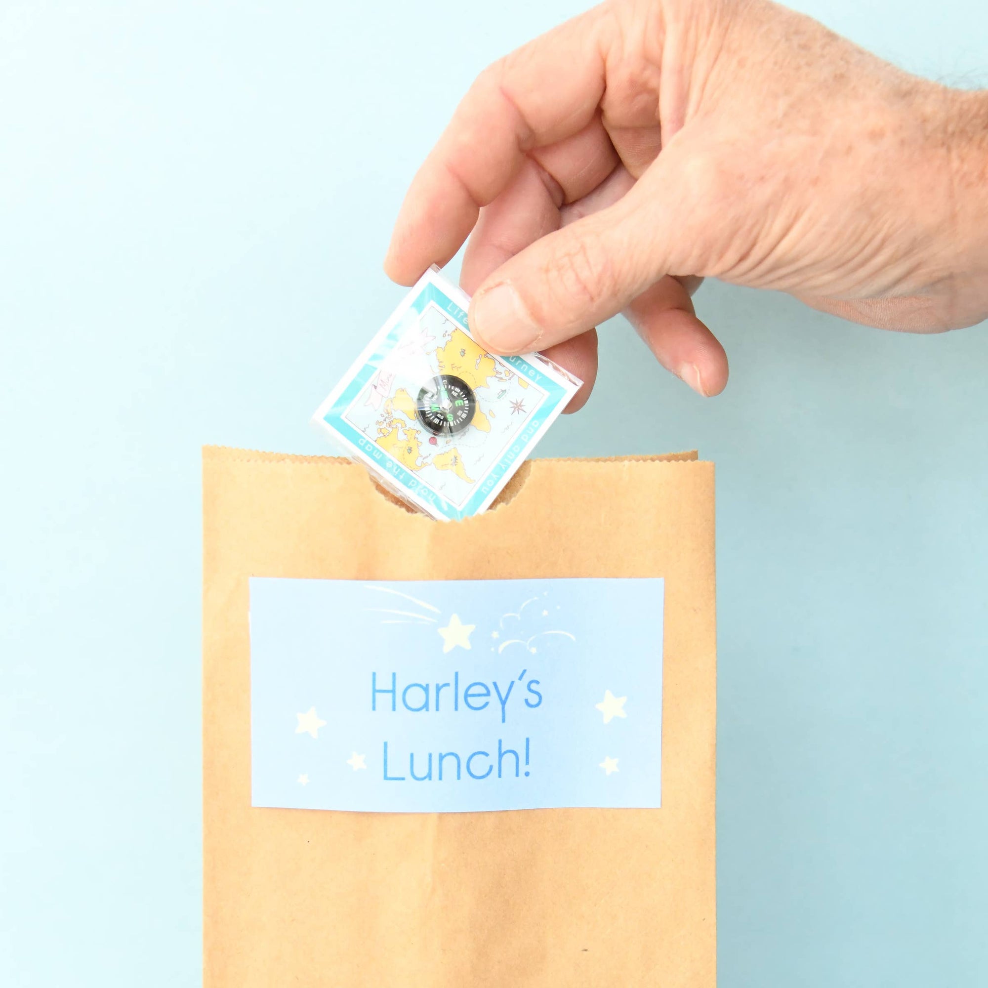 Hand placing a lunchbox label on a cardboard box with a blue background
