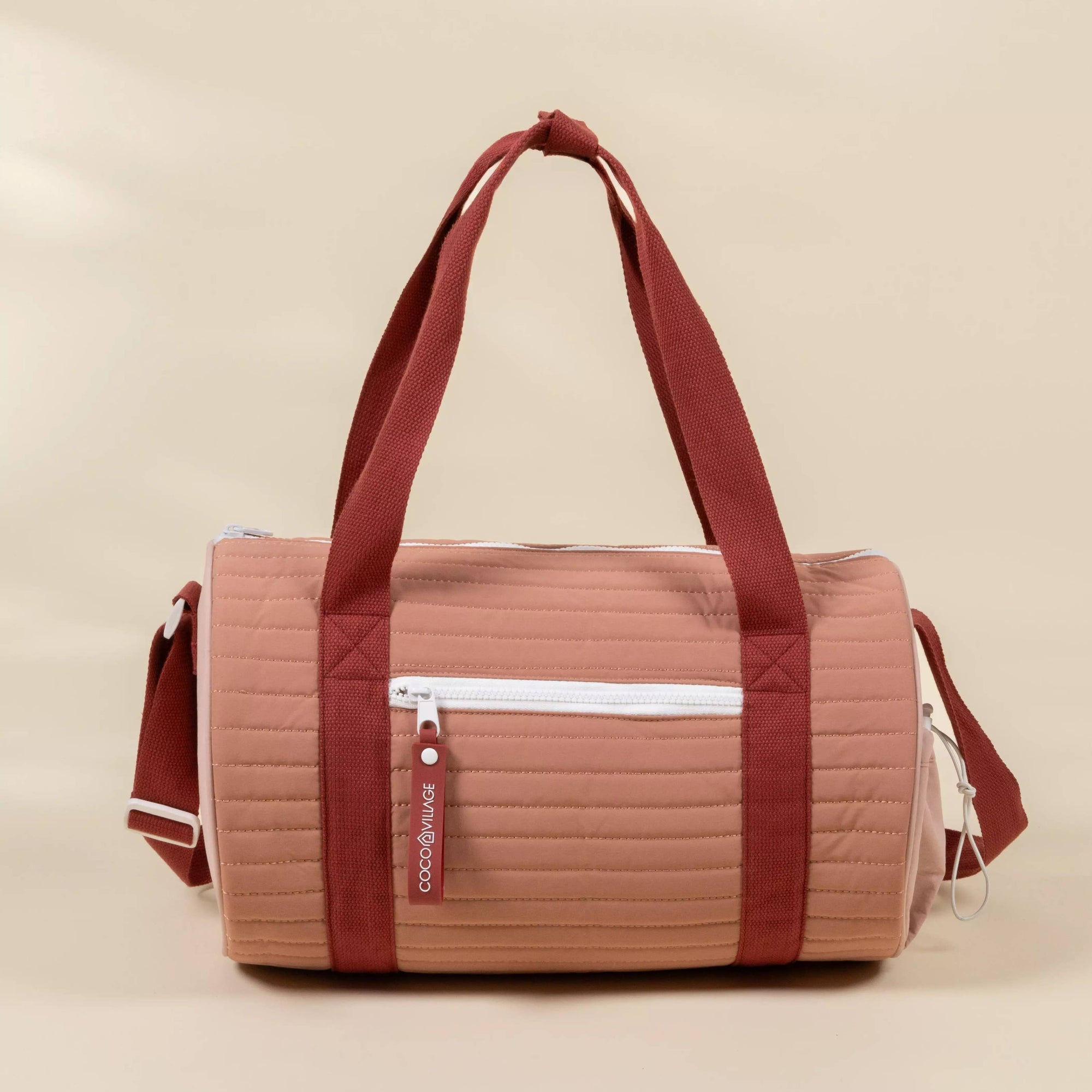 Quilted duffel bag with red straps on a beige background