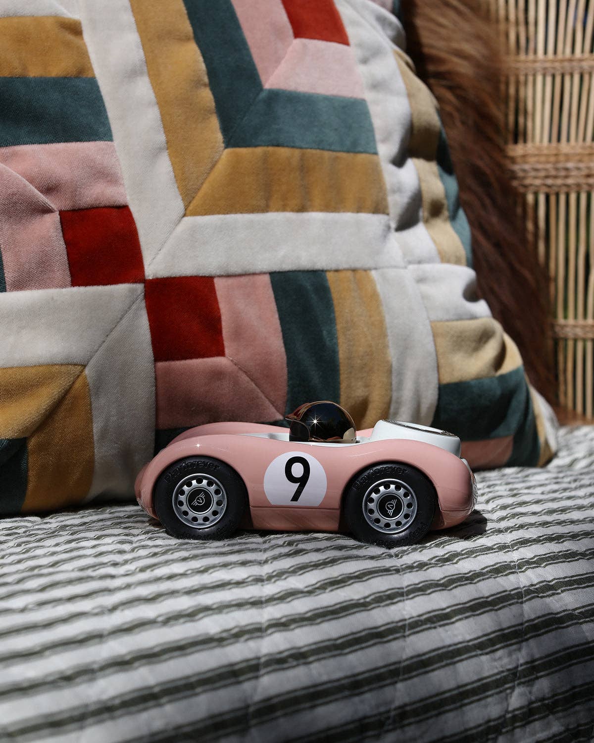 Pink toy car with number 9 on a striped surface with a patchwork quilt in the background